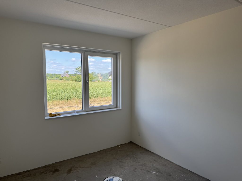 Lichte kamer met gladde wanden en een raam dat uitkijkt over een maisveld