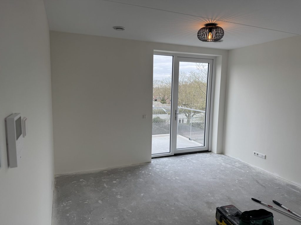 Nieuwbouwkamer met gladde witte wanden en openslaande deuren naar een balkon