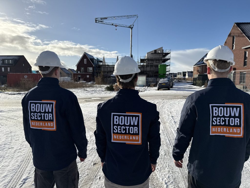 Drie vakmensen van Bouwsector Nederland met witte helm kijken naar woningen in aanbouw